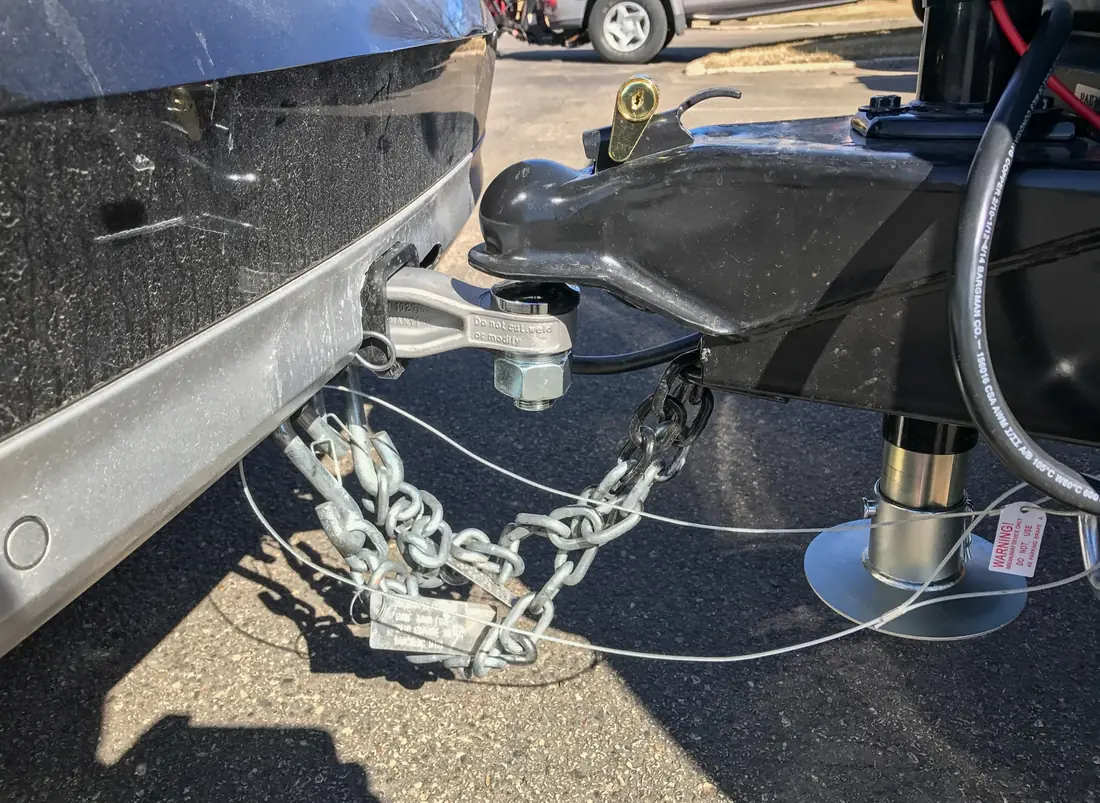 Ball coupler latched and locked on a hitch ball, with crossed safety chains, a breakaway cable and the tongue jack foot.