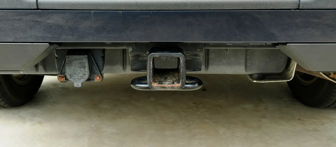 Rear of a pickup showing a square 2-inch receiver hitch and a 7-pin trailer connector mounted beside it.