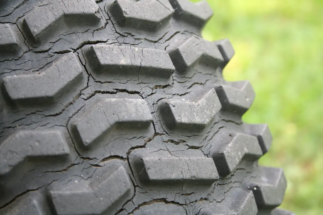 Close-up of a lugged tire with deep tread and a web of weather cracks across the rubber.